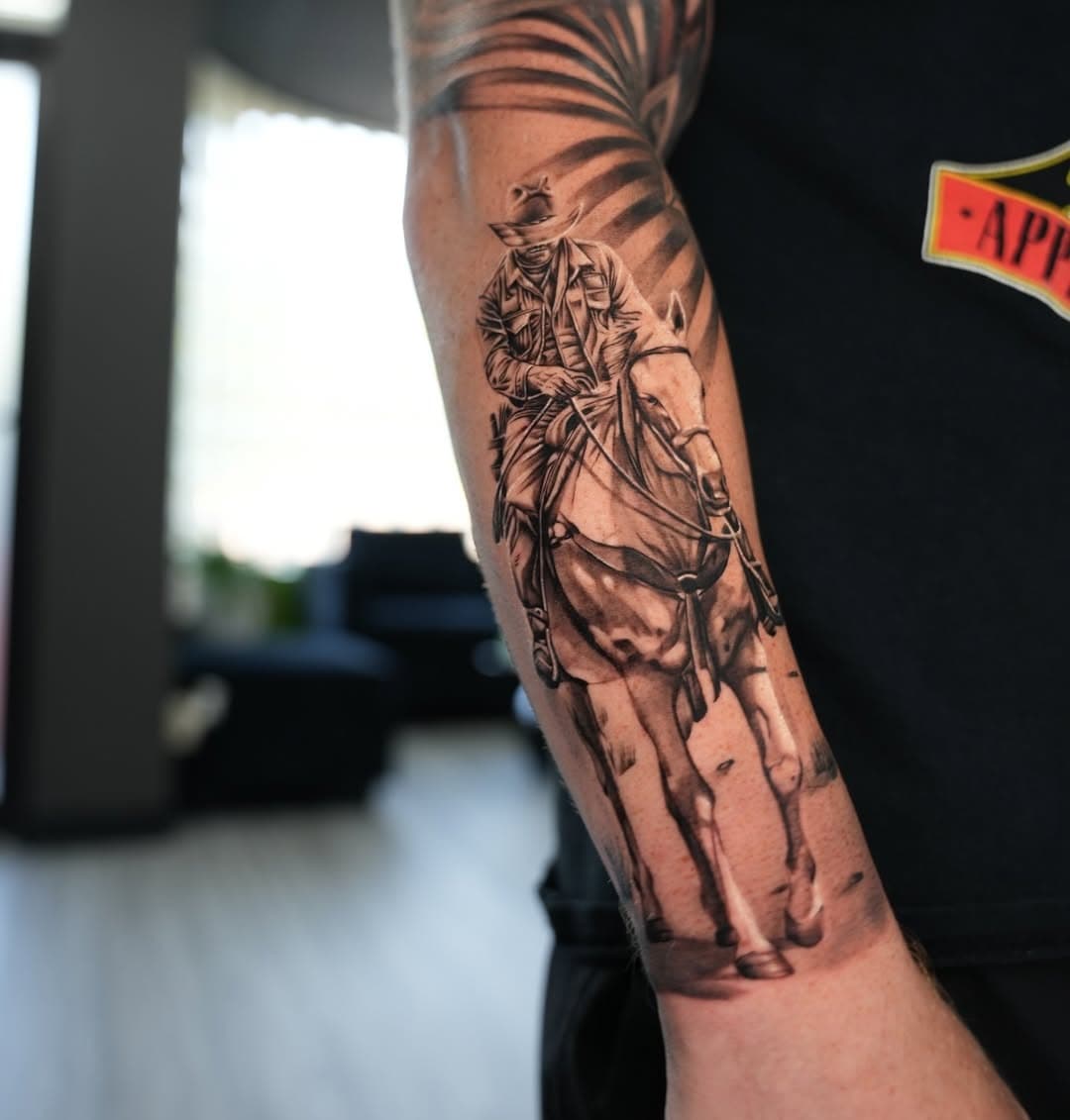 Black and grey realistic cowboy on horseback tattoo on forearm by Ink Theory