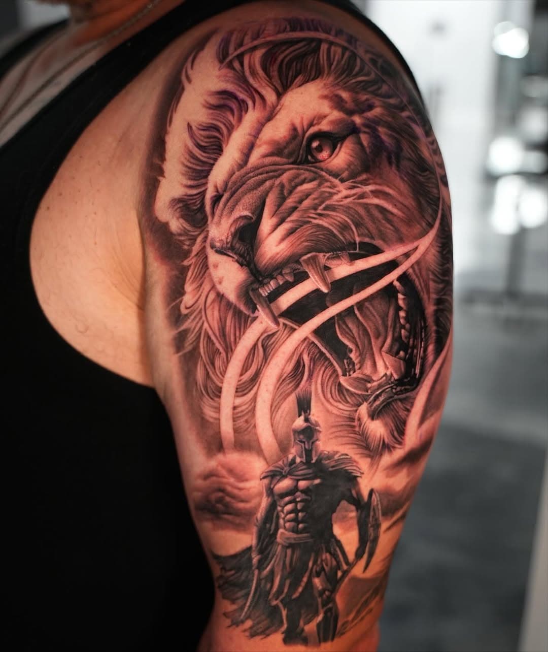 Black and grey roaring lion with Spartan warrior tattoo on shoulder by Ink Theory